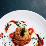 Plate of spaghetti with tomato sauce and garnished with fresh tomatoes and herbs.
