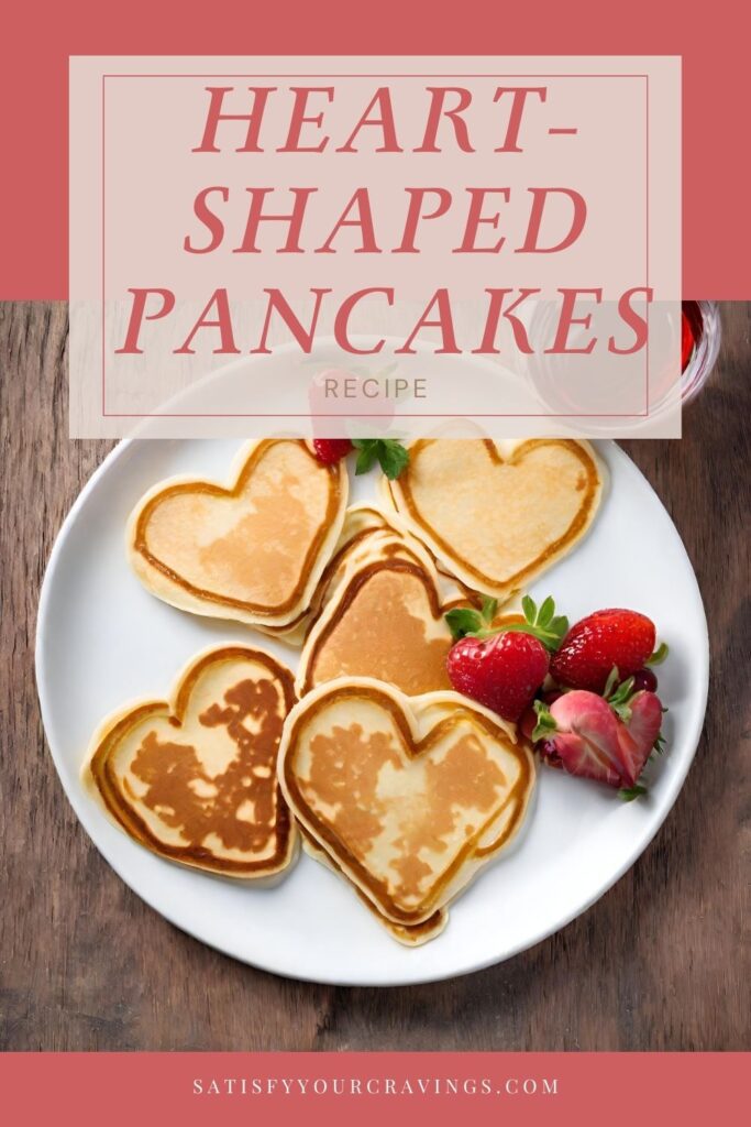 A promotional image for a recipe on SatisfyYourCravings.com featuring a plate of heart-shaped pancakes. The pancakes are golden brown, with some displaying lighter heart patterns due to the pour of the batter. Accompanying the pancakes are fresh strawberries with vibrant green leaves. The background is a warm wooden texture, providing a rustic feel. At the top, a salmon-colored banner with white text reads "HEART SHAPED PANCAKES RECIPE," and the website name is placed at the bottom. The image is styled to invite a sense of homemade warmth and love.