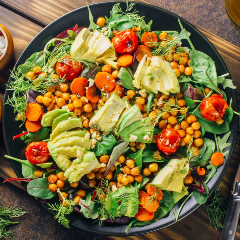 A vibrant Avocado Chickpea Salad with roasted chickpeas, sliced avocado, cherry tomatoes, and mixed greens, served on a black plate.