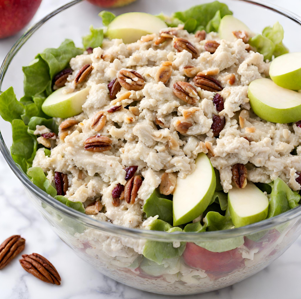 A fresh and appetizing bowl of Apple Pecan Chicken Salad, featuring succulent shredded chicken, crisp apple slices, and toasted pecans on a bed of lush green lettuce, garnished with dried cranberries for a hint of tart sweetness. Perfect for a healthy chicken salad recipe search.