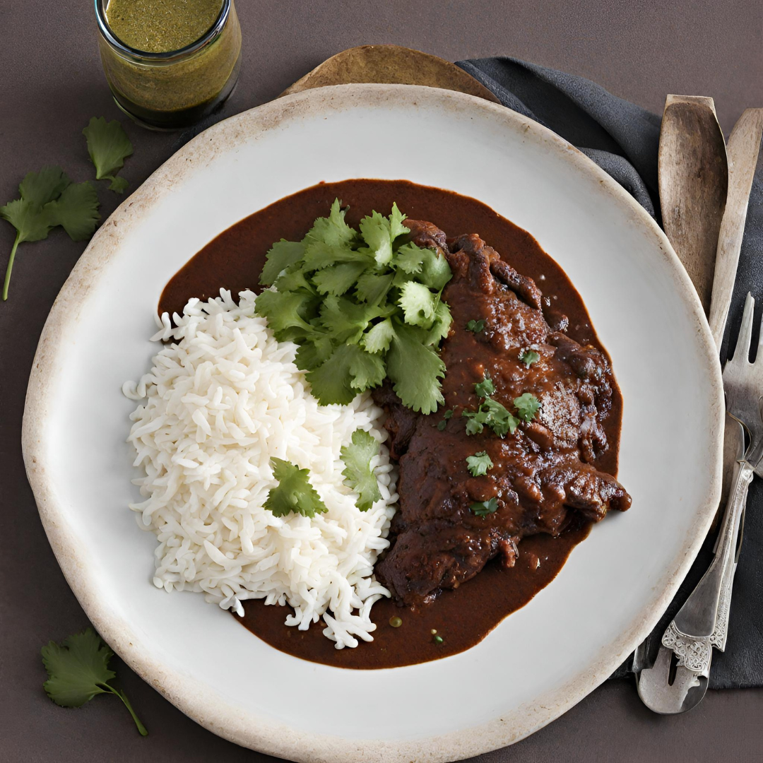 Delicious Chicken Mole Poblano served with white rice and garnished with fresh cilantro, presented on a rustic ceramic plate with a green sauce in the background.