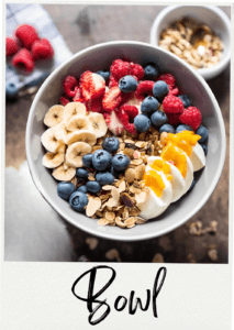 Gourmet Muesli Breakfast Bowl topped with blueberries, raspberries, sliced strawberries, banana, mango. And eggs, garnished with almond slices.