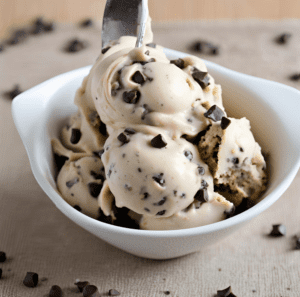 A bowl of cookie dough ice cream sprinkled with chocolate chips, with a spoon scooping out a serving.