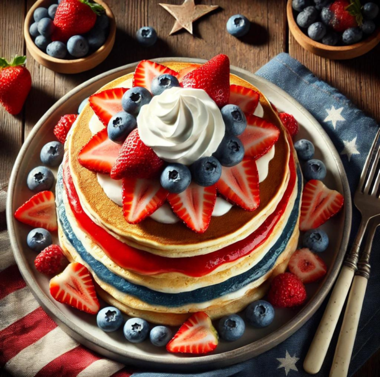 Overhead view of a stack of red, white, and blue pancakes topped with fresh strawberries and blueberries.