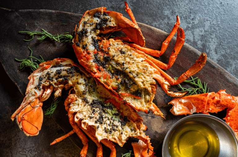 Delicious grilled lobster tails with garlic herb butter served on a wooden board, accompanied by a bowl of melted butter. Perfect for a gourmet summer BBQ. Get the full recipe on Satisfy Your Cravings. #GrilledLobster #SeafoodRecipes #SummerBBQ #SatisfyYourCravings