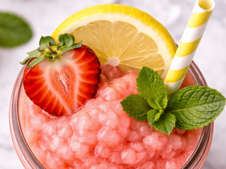 Top view of a strawberry lemonade slushie with a lemon wheel, strawberry half, mint sprig, and striped straw.