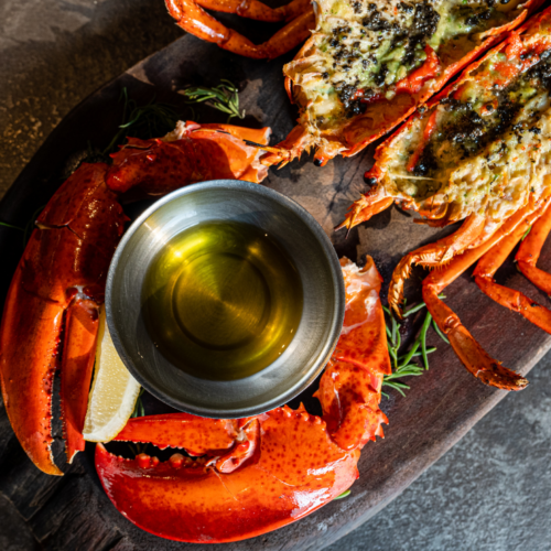 Grilled lobster tails with garlic herb butter served on a wooden board with a bowl of melted butter, perfect for summer BBQs and gourmet seafood lovers.