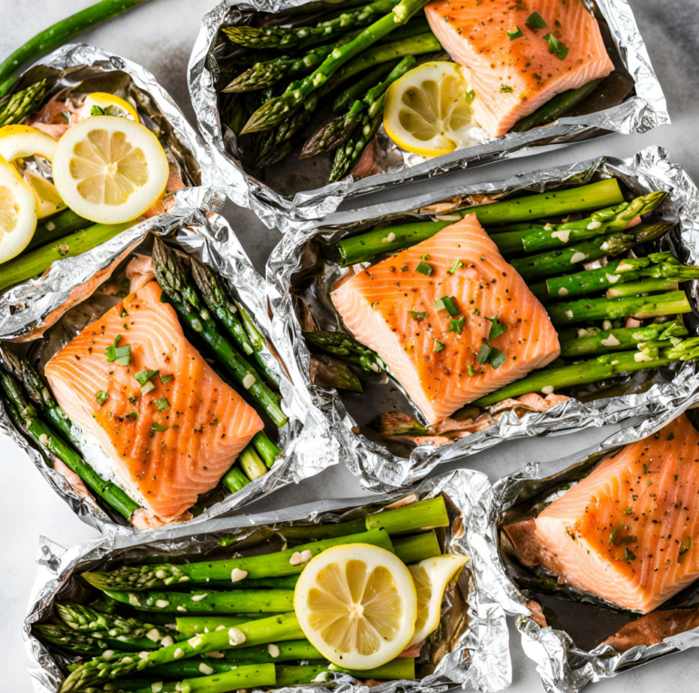 Five salmon fillets with asparagus and lemon slices in foil packets, ready to be cooked.