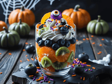 Halloween fruit parfait with whipped cream, blueberries, kiwi, and oranges topped with candy eye sprinkles.