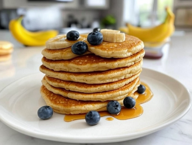 A plate of banana oatmeal pancakes topped with fresh blueberries and banana slices, drizzled with maple syrup.