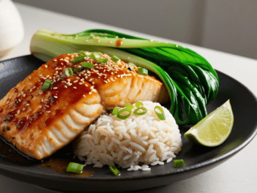 A close-up of a miso-glazed cod fillet, perfectly seared with a thick, glossy miso glaze, topped with sesame seeds and green onions, alongside steamed bok choy and jasmine rice on a dark ceramic plate.