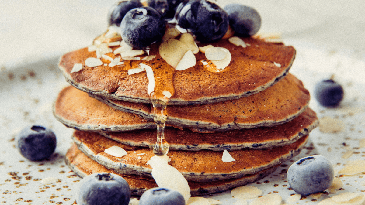 Stack of blueberry pancakes topped with fresh blueberries, sliced almonds, and a drizzle of honey.